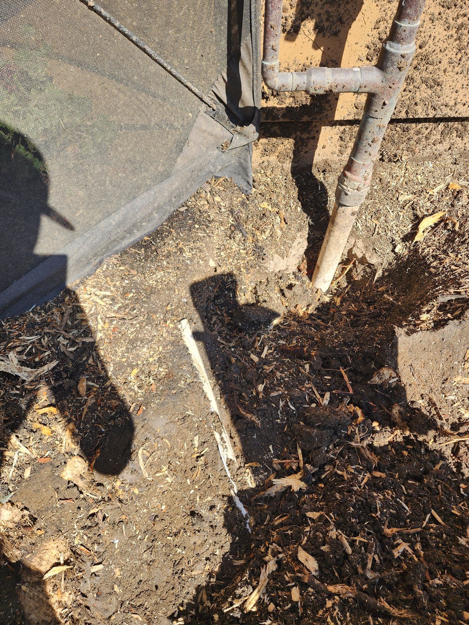 Shadow of a person and chair on a dirt ground scattered with small brown debris.