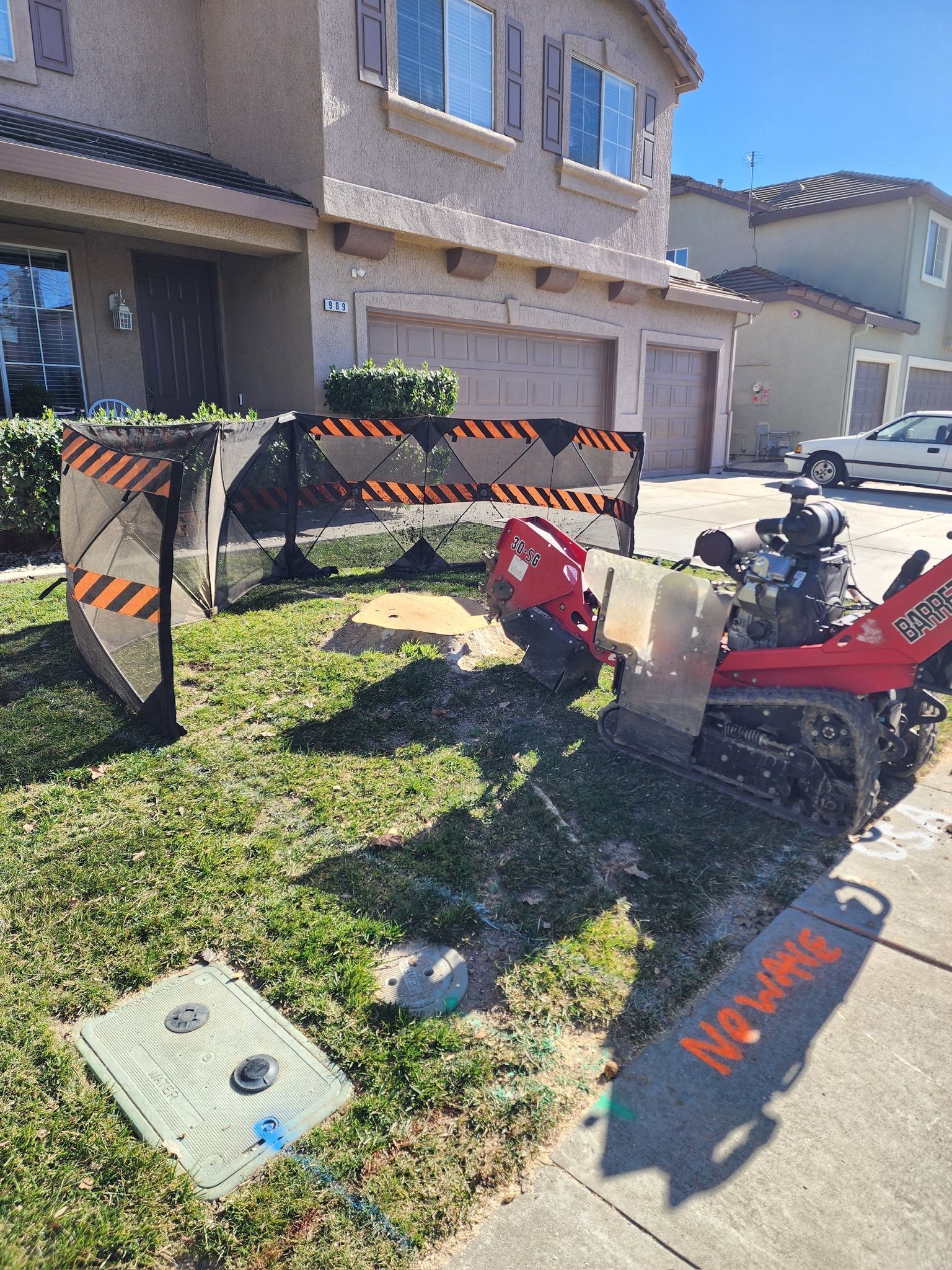 Red construction machine with barrier on residential lawn. A street and a house are in the background.
