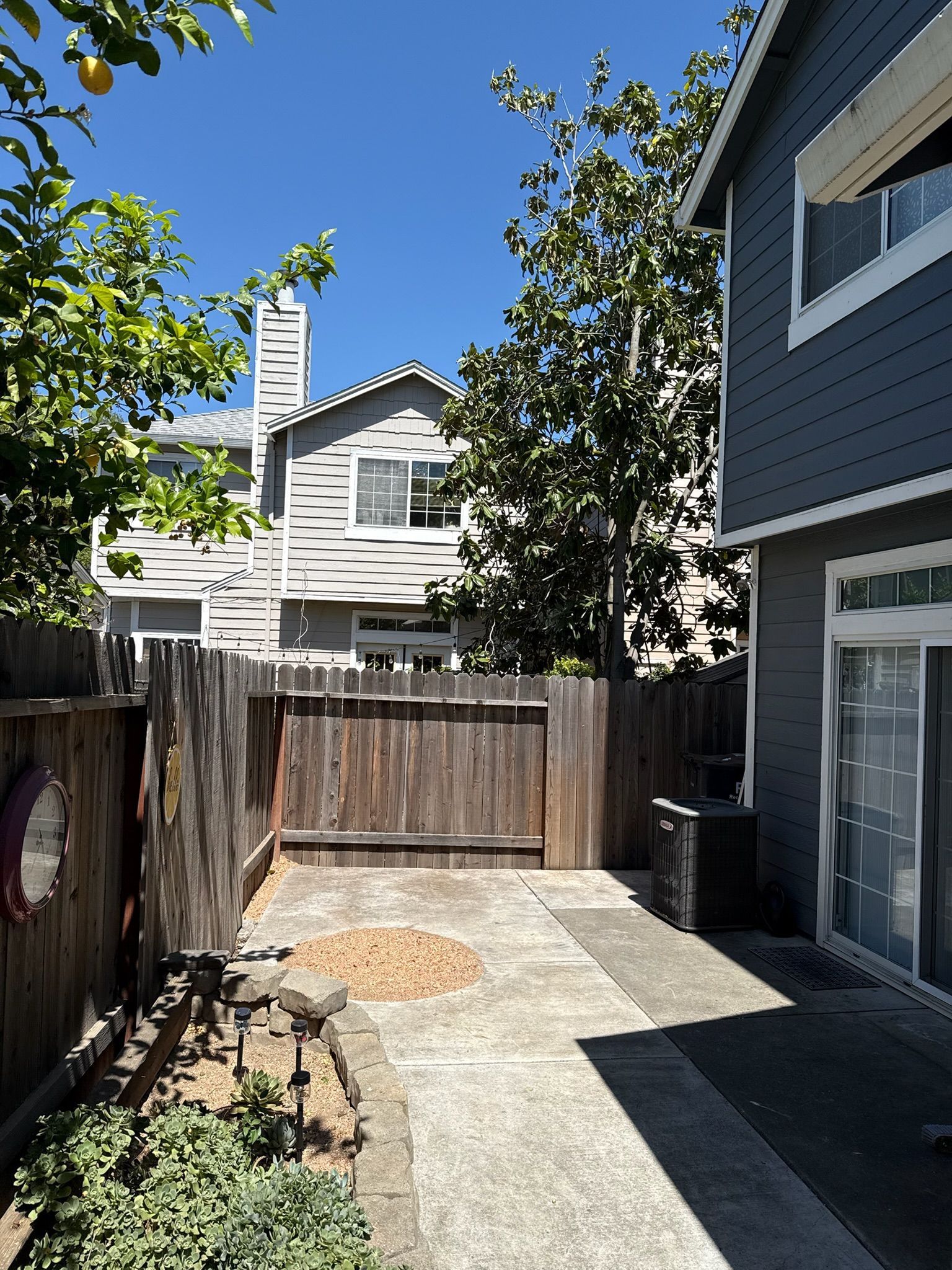 Backyard patio with wooden fence, concrete path, and two-story house.