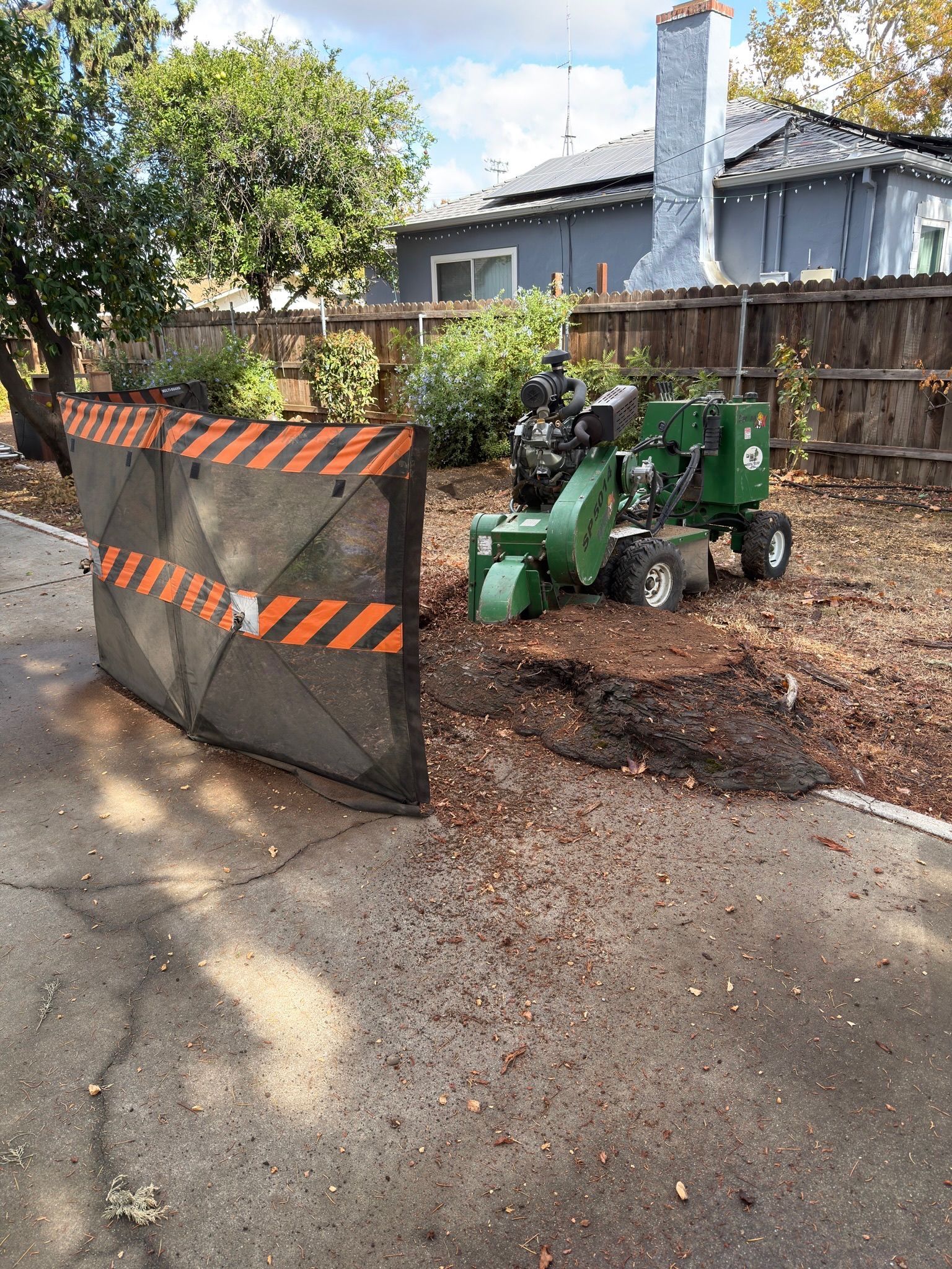 A stump grinder with safety shield grinding a tree stump in a yard.