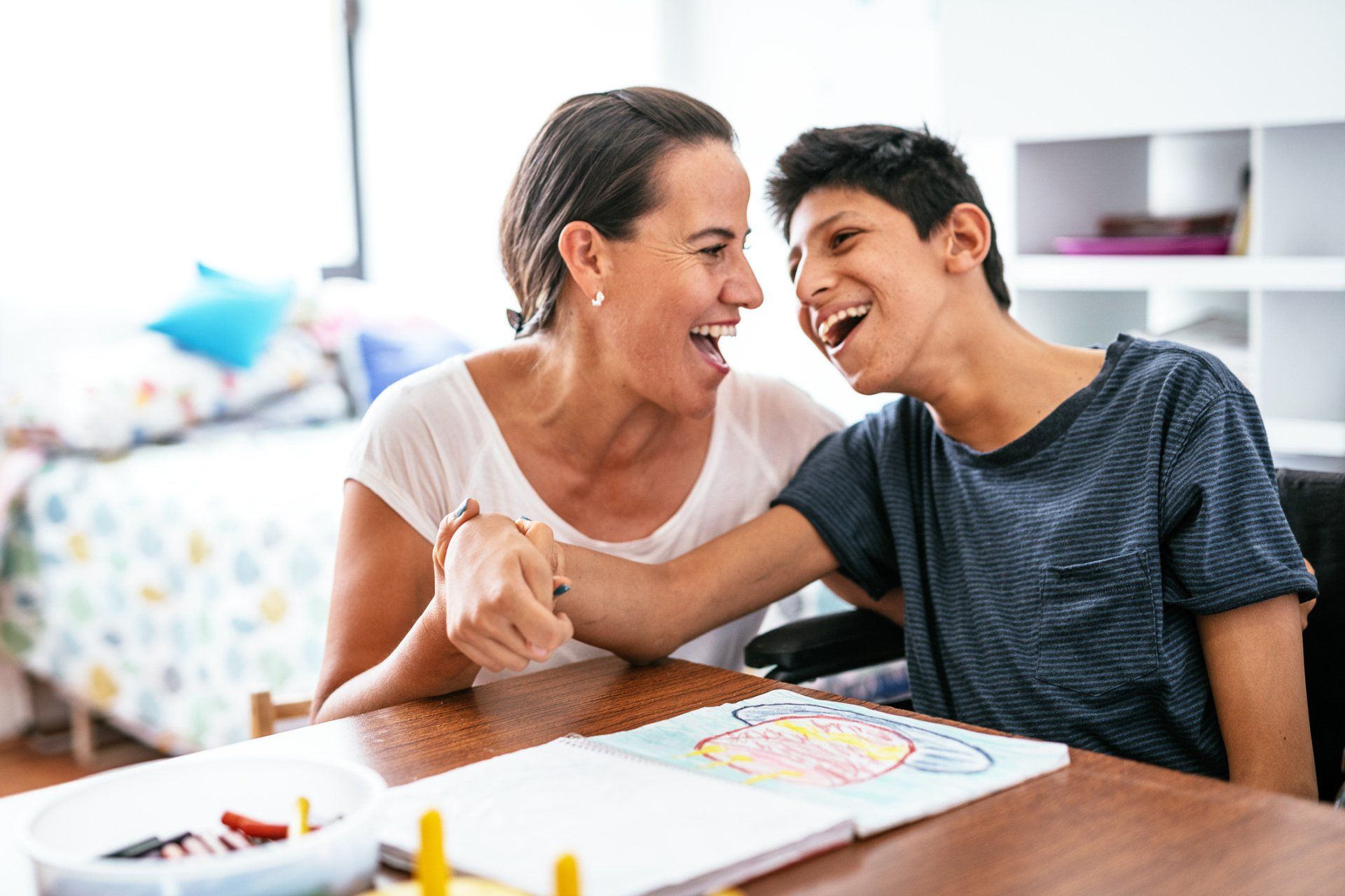 A woman is sitting at a table with a boy in a wheelchair.