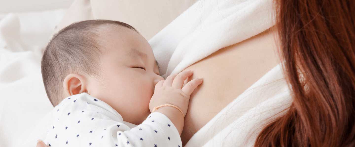 A woman is breastfeeding her baby on a bed.