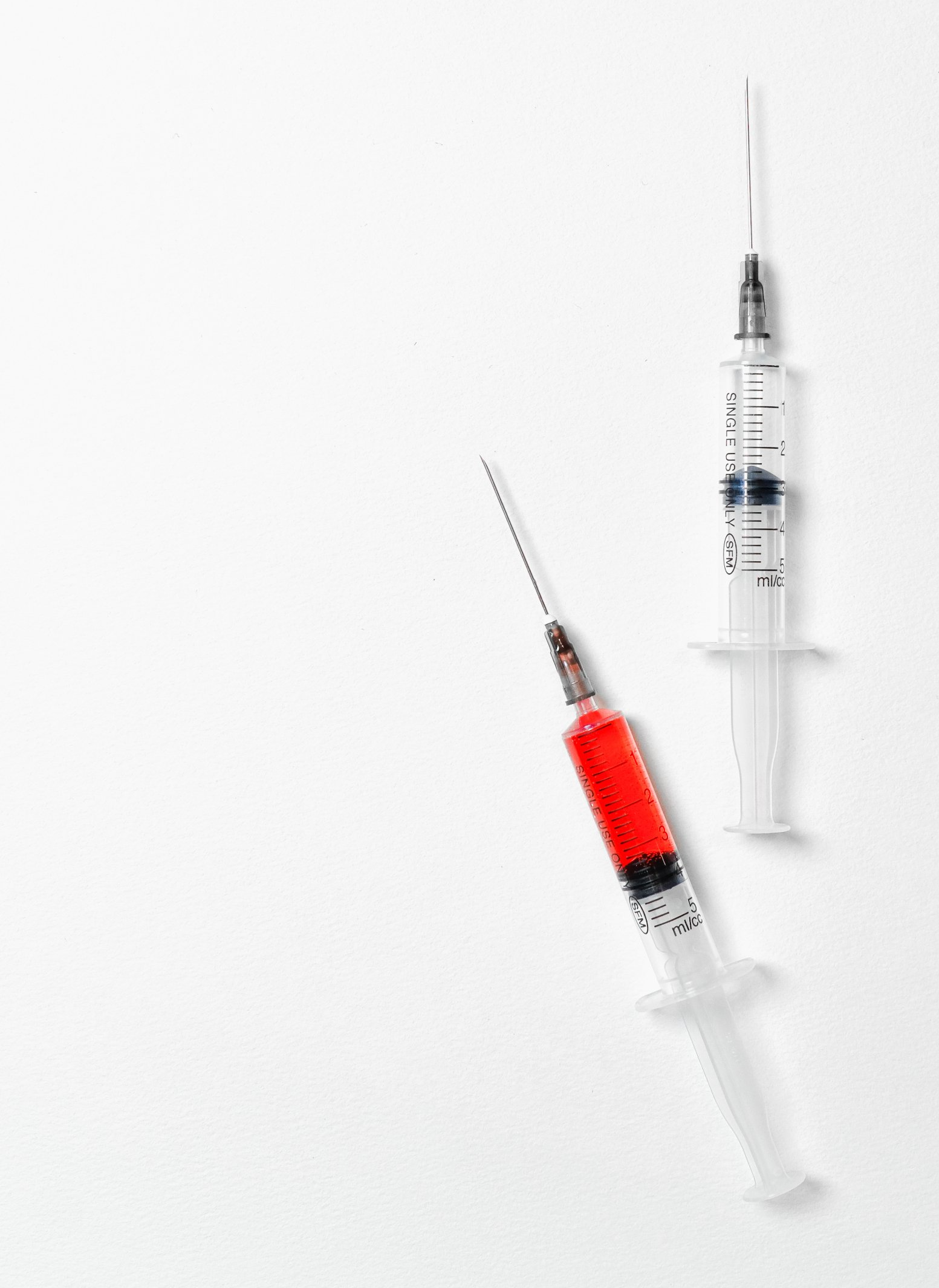 Two syringes with red liquid in them on a white background.