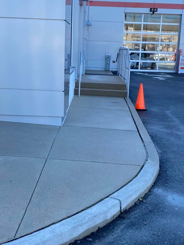 Sidewalk ramp with an orange traffic cone next to a building entrance.