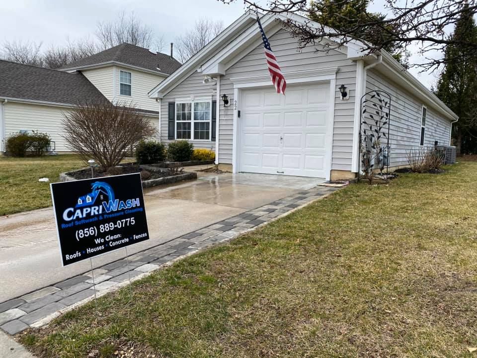 A house with a clean, wet driveway and a sign advertising Capri Clean, with an American flag displayed.