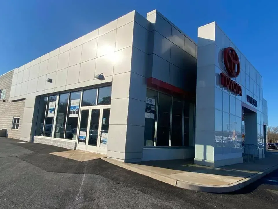 Toyota dealership exterior with a modern, silver facade and large windows under a blue sky.