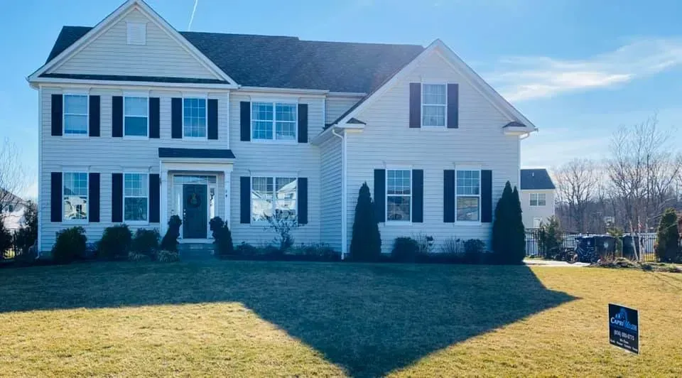 Two-story beige house with black shutters, on a sunny day. 