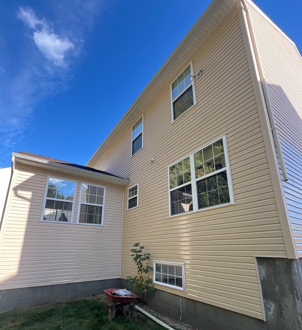 Beige vinyl-sided house with multiple windows against a blue sky, gutter and short green grass.