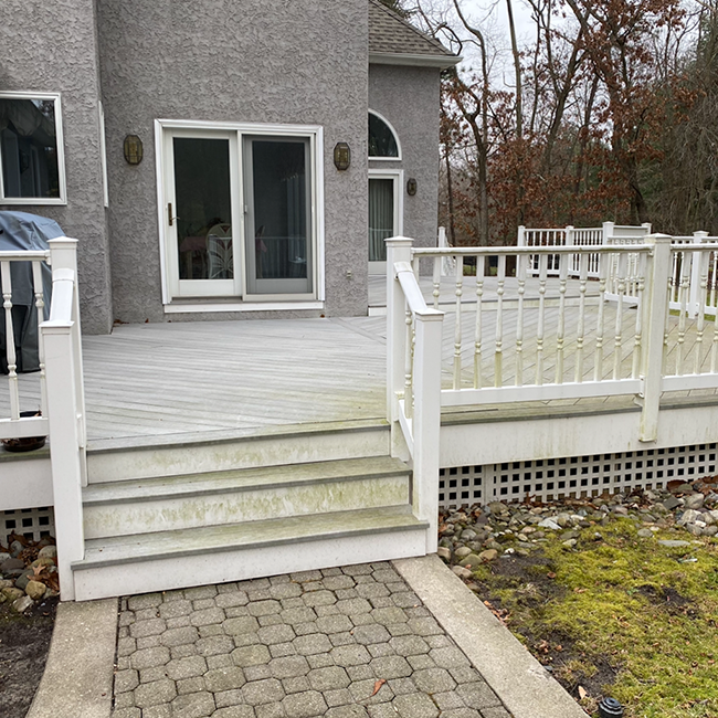 Backyard deck with white railings and stairs, connecting to a gray house, set on a stone path.