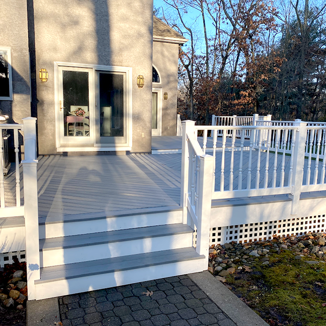 Grey and white deck with steps leading to a house. White railings and lattice surround the deck.