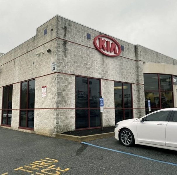 Kia dealership exterior with a white car parked in front.