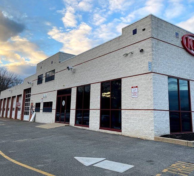 Exterior of a Kia dealership building with large windows and a service bay. Cloudy sky overhead.