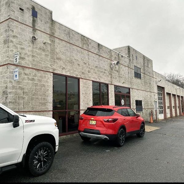 A red SUV and a white pickup truck parked in front of a light gray commercial building with windows.