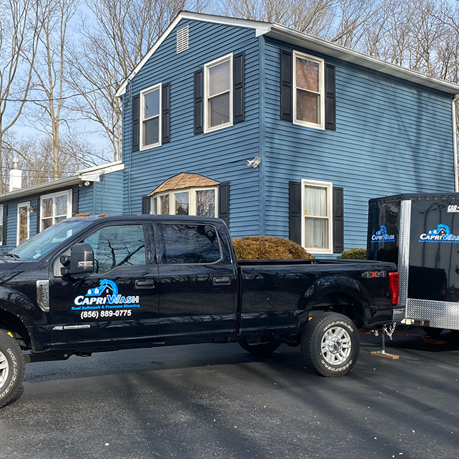 Black truck and trailer parked in front of a blue house with mulch in the truck bed.