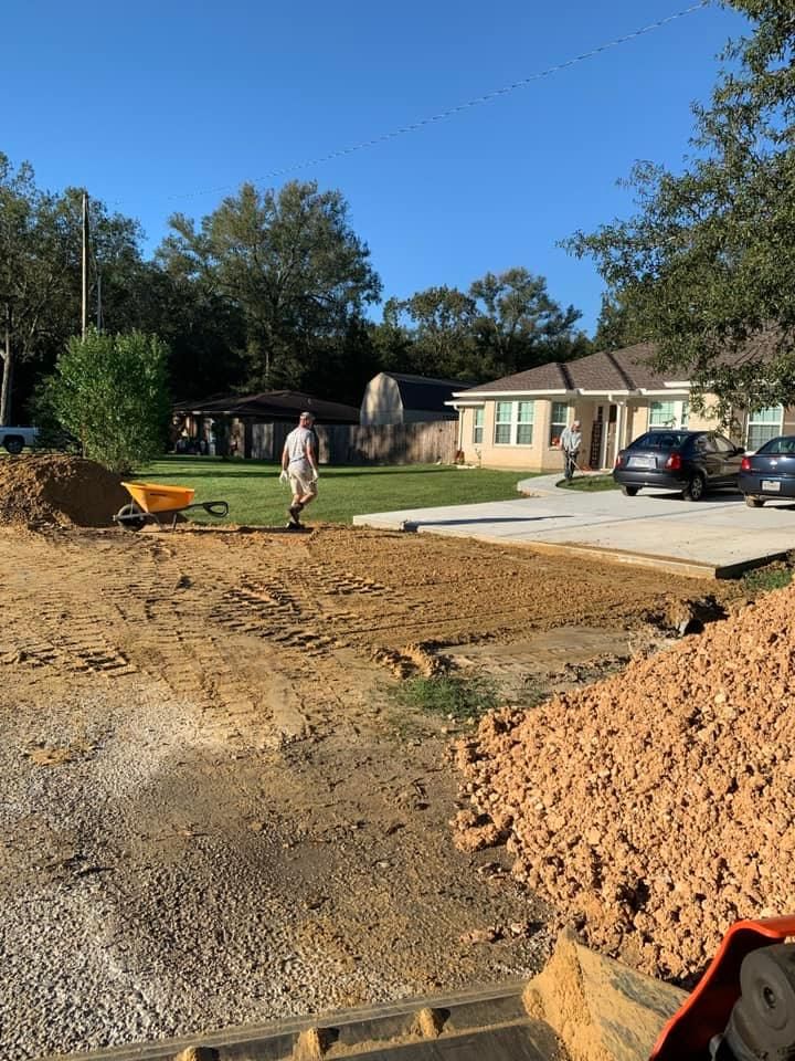 Construction site. Man walking on dirt. House in background. Wheelbarrow and pile of dirt visible.
