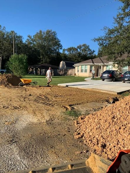 Construction site: person walking on dirt, house in background, small equipment, blue sky.