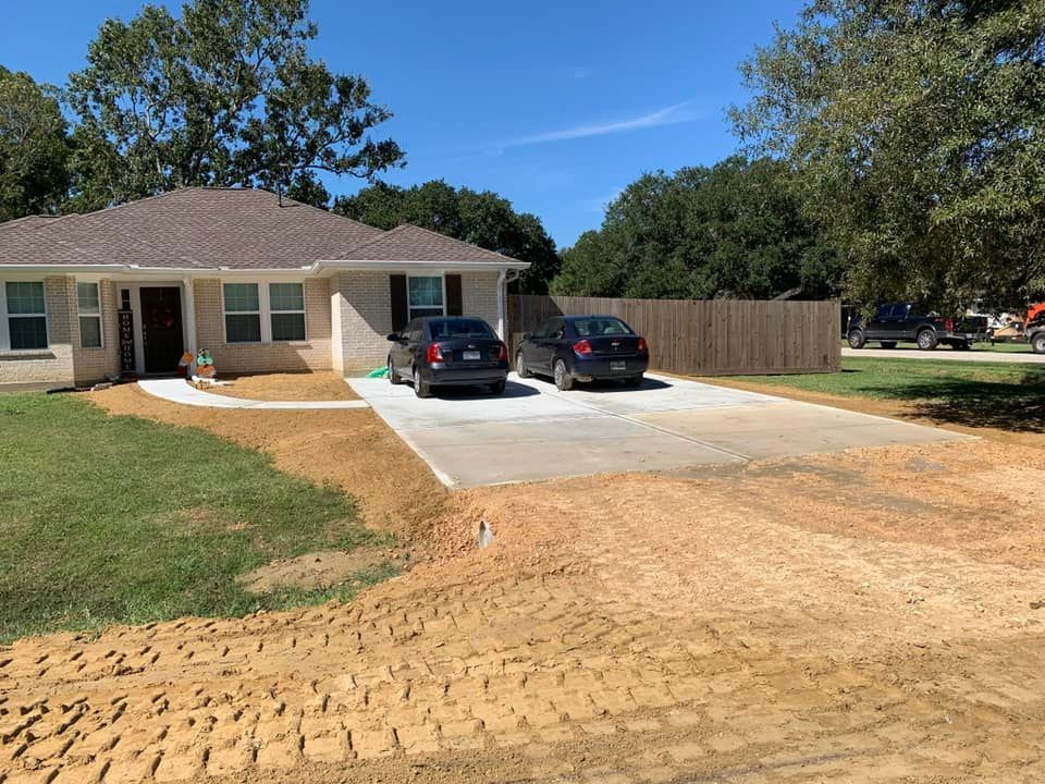 A single-story house with a concrete driveway. Two cars are parked. The lawn has exposed dirt.