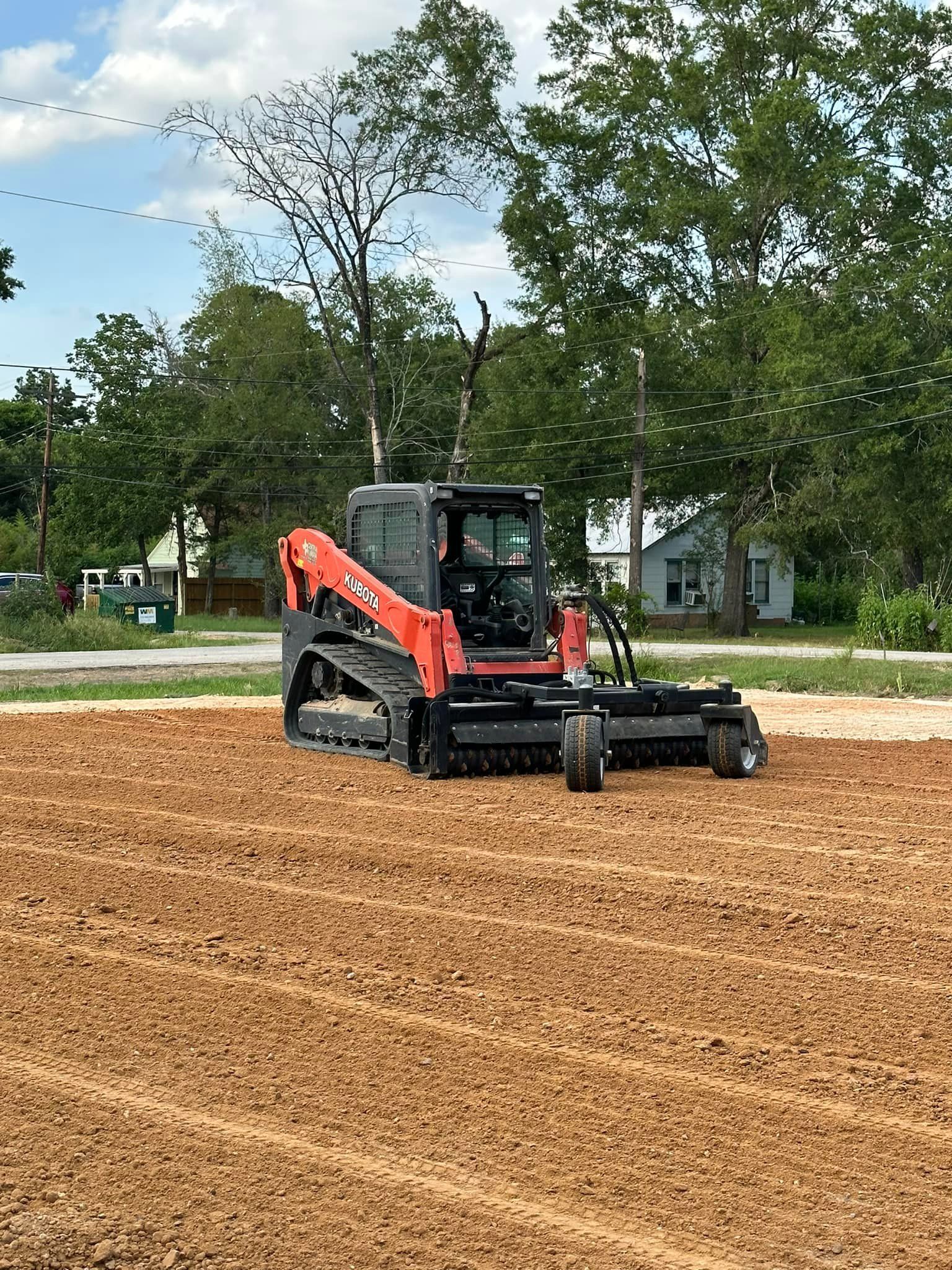 Orange and black track skid steer leveling a brown dirt lot.