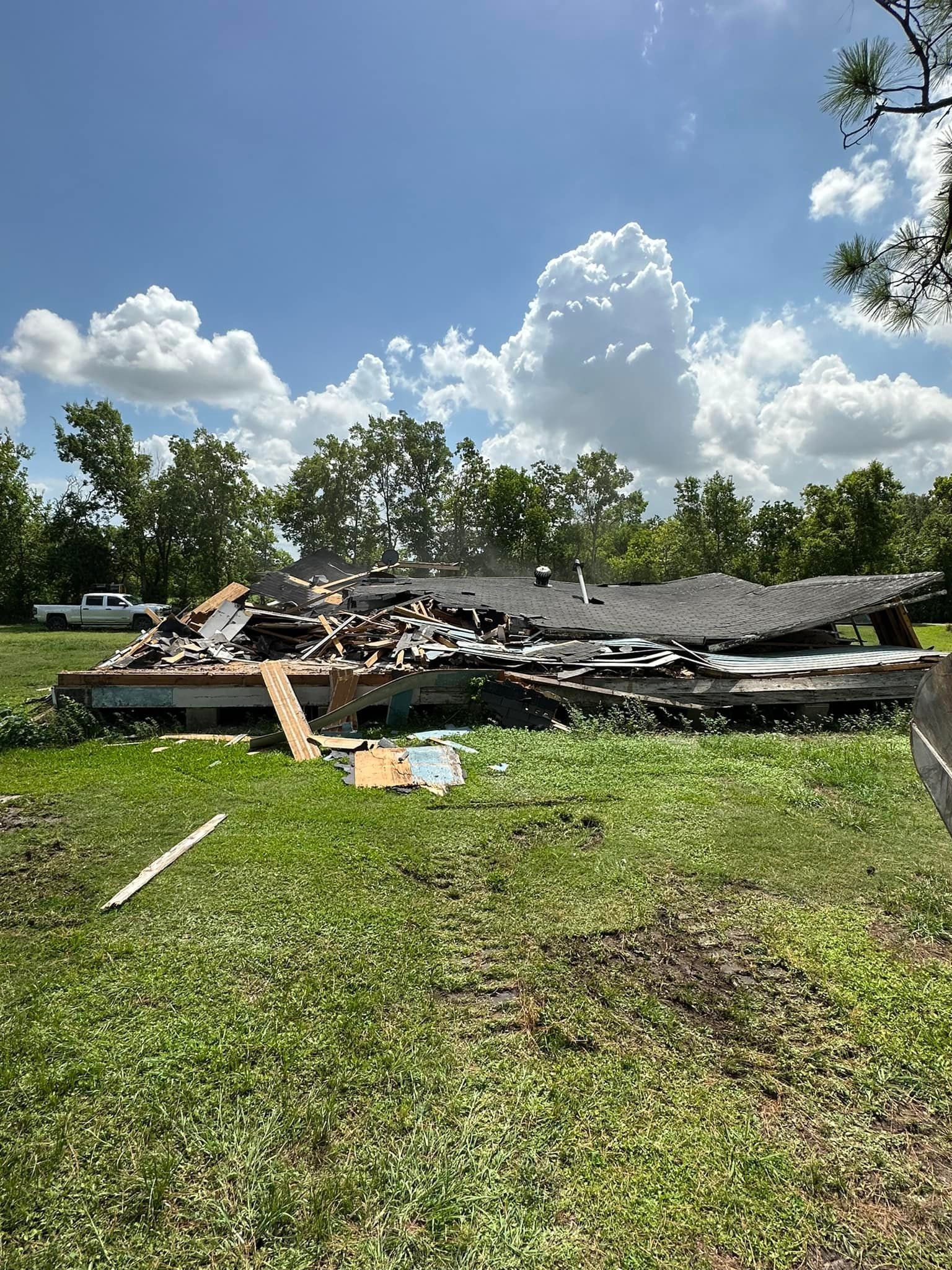 A destroyed house on a grassy field under a sunny sky with scattered clouds.