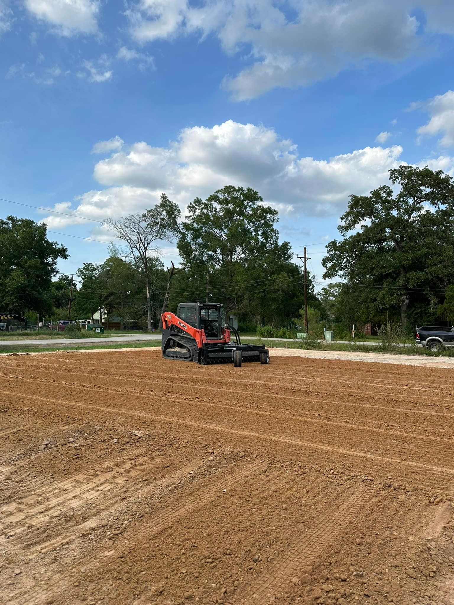 Red skid steer on a freshly tilled field, under a partly cloudy sky.