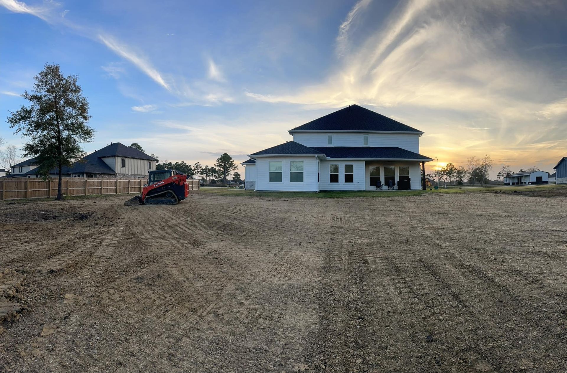 A white house with a dark roof on a dirt lot under a cloudy sky.