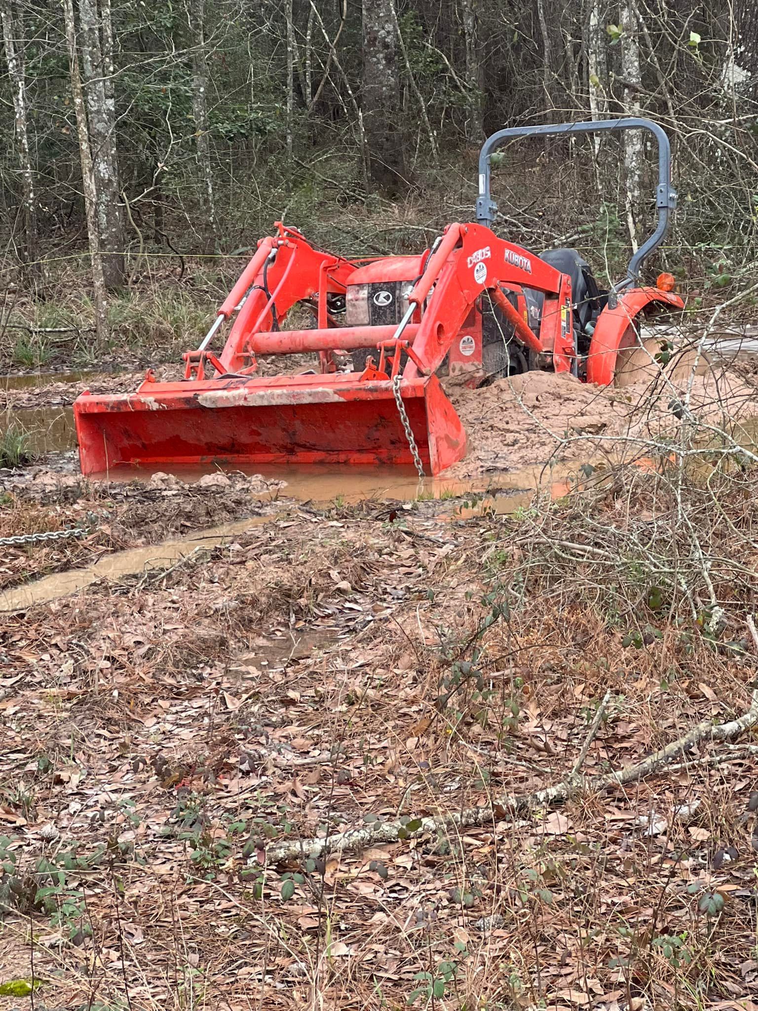 Red tractor stuck in mud in a wooded area, bucket down.