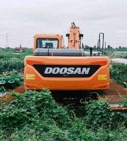 Orange tractor stuck in mud in a wooded area.