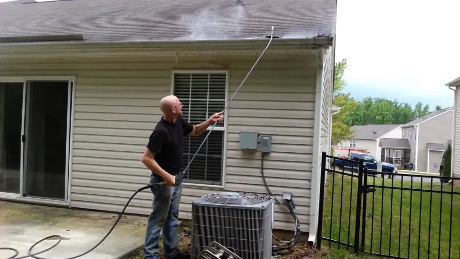 Professional using extension pole to soft wash home siding.