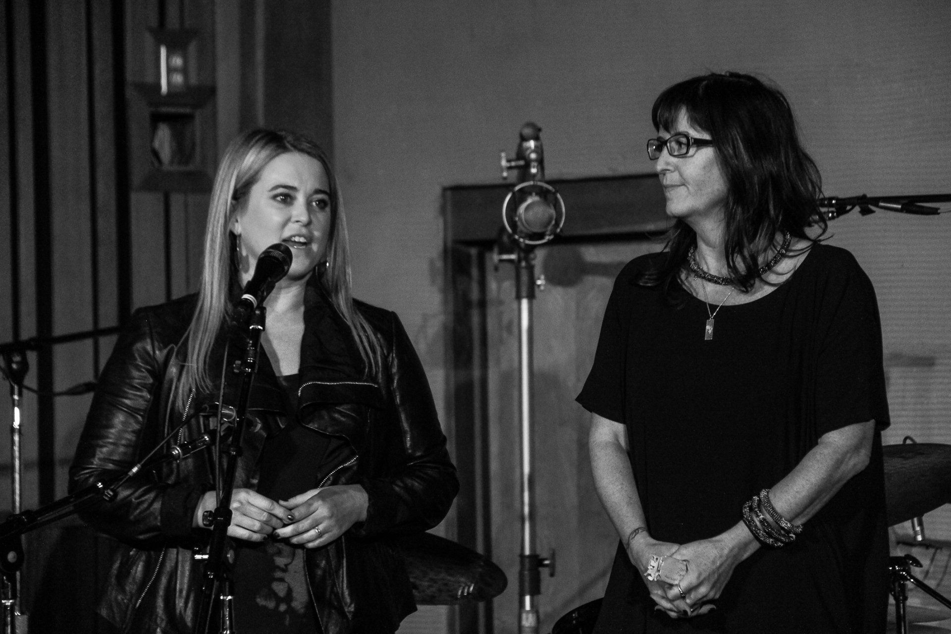 Two women are singing into microphones in a black and white photo.