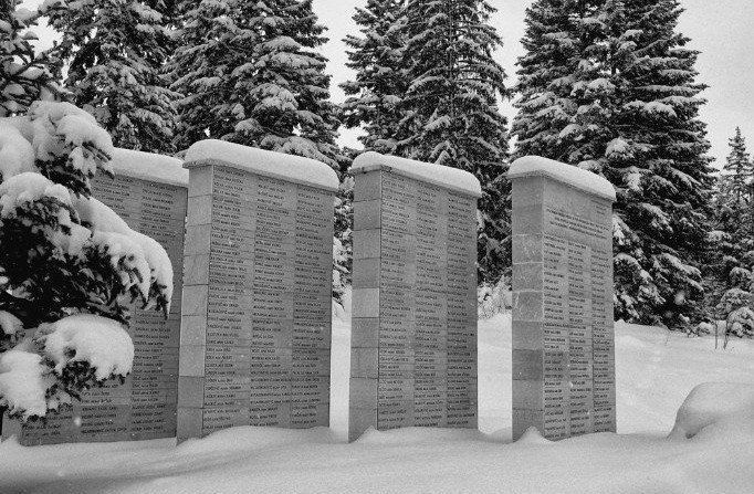 gray monument stones with writing on them, surrounded by snow and evergreen trees