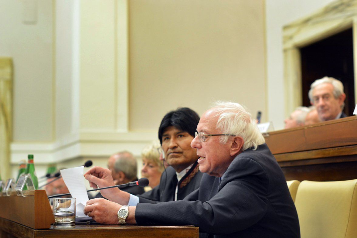 A man in a suit is sitting at a table in front of a microphone holding a piece of paper.