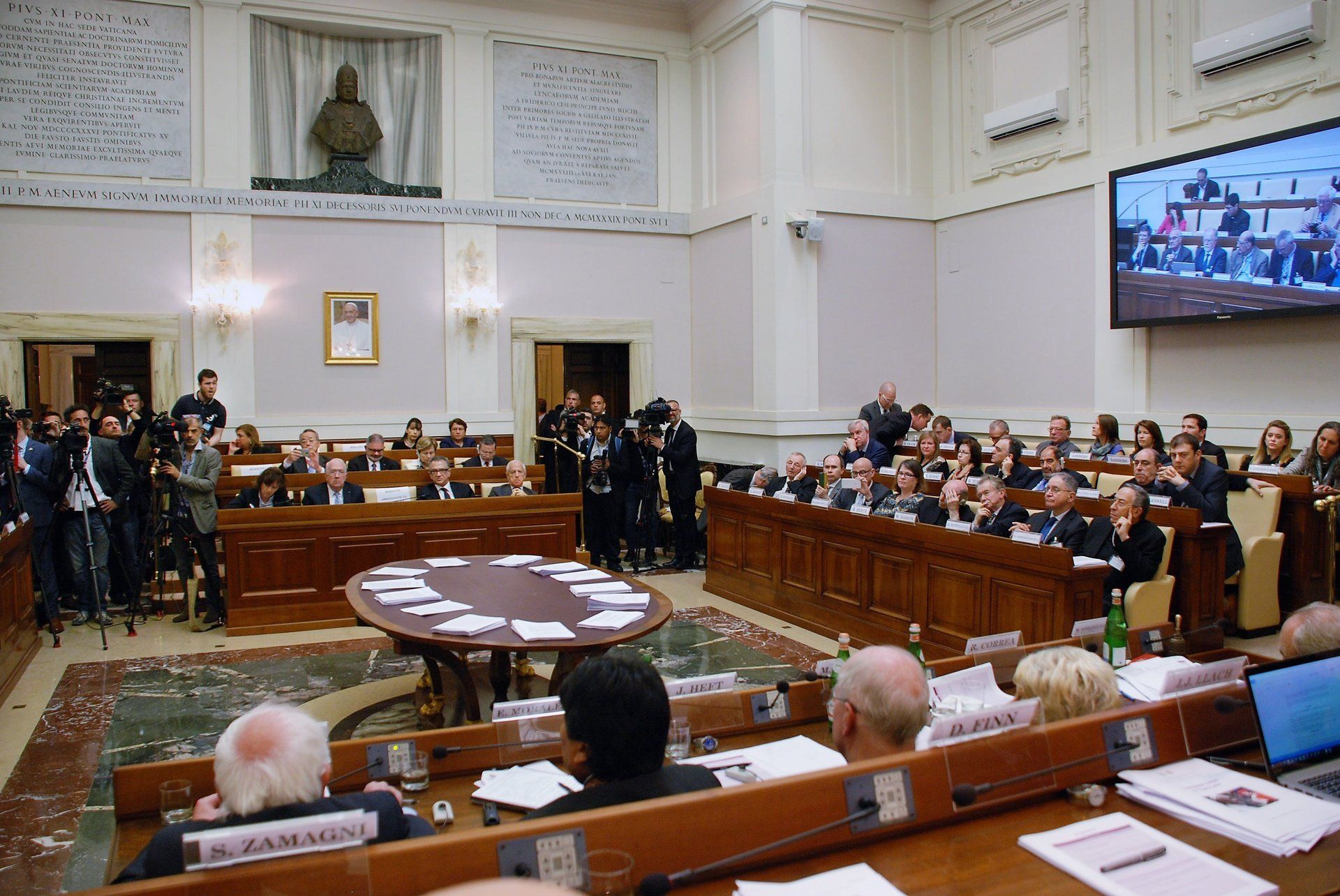 A group of people are sitting in a room with a large screen behind them