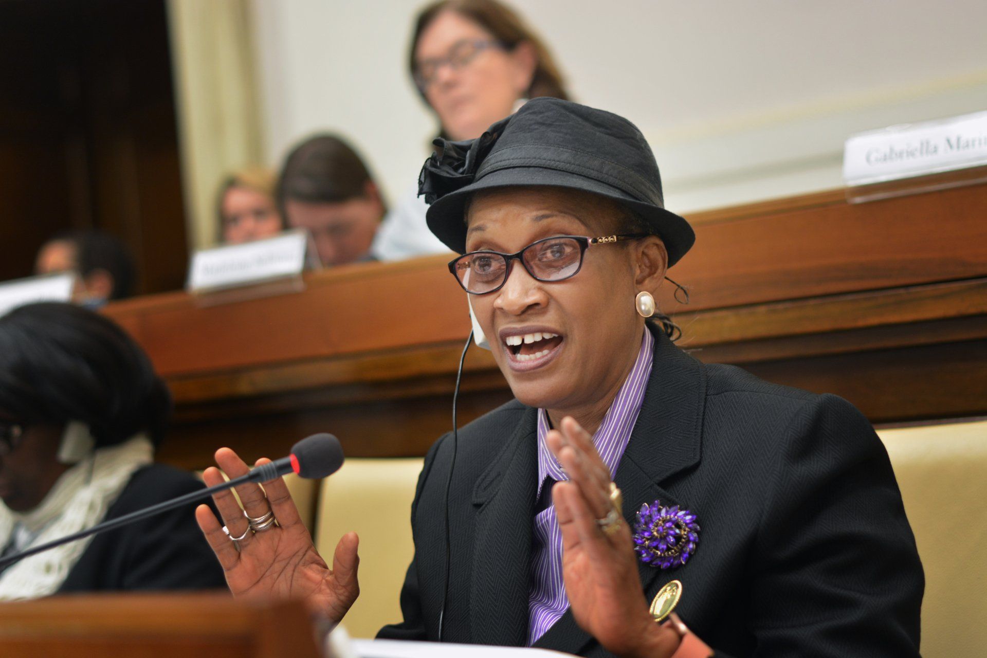 A woman wearing a hat and glasses is speaking into a microphone