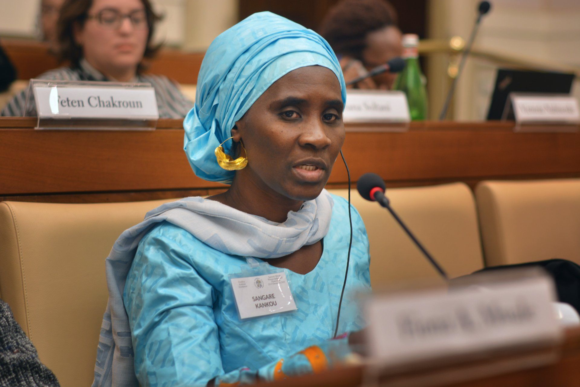 A woman in a blue turban is speaking into a microphone