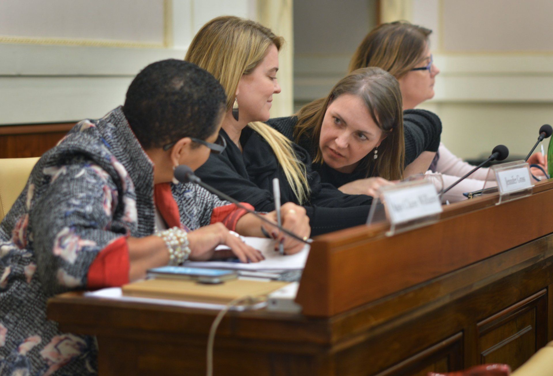 A group of women are sitting at a table writing on a piece of paper.