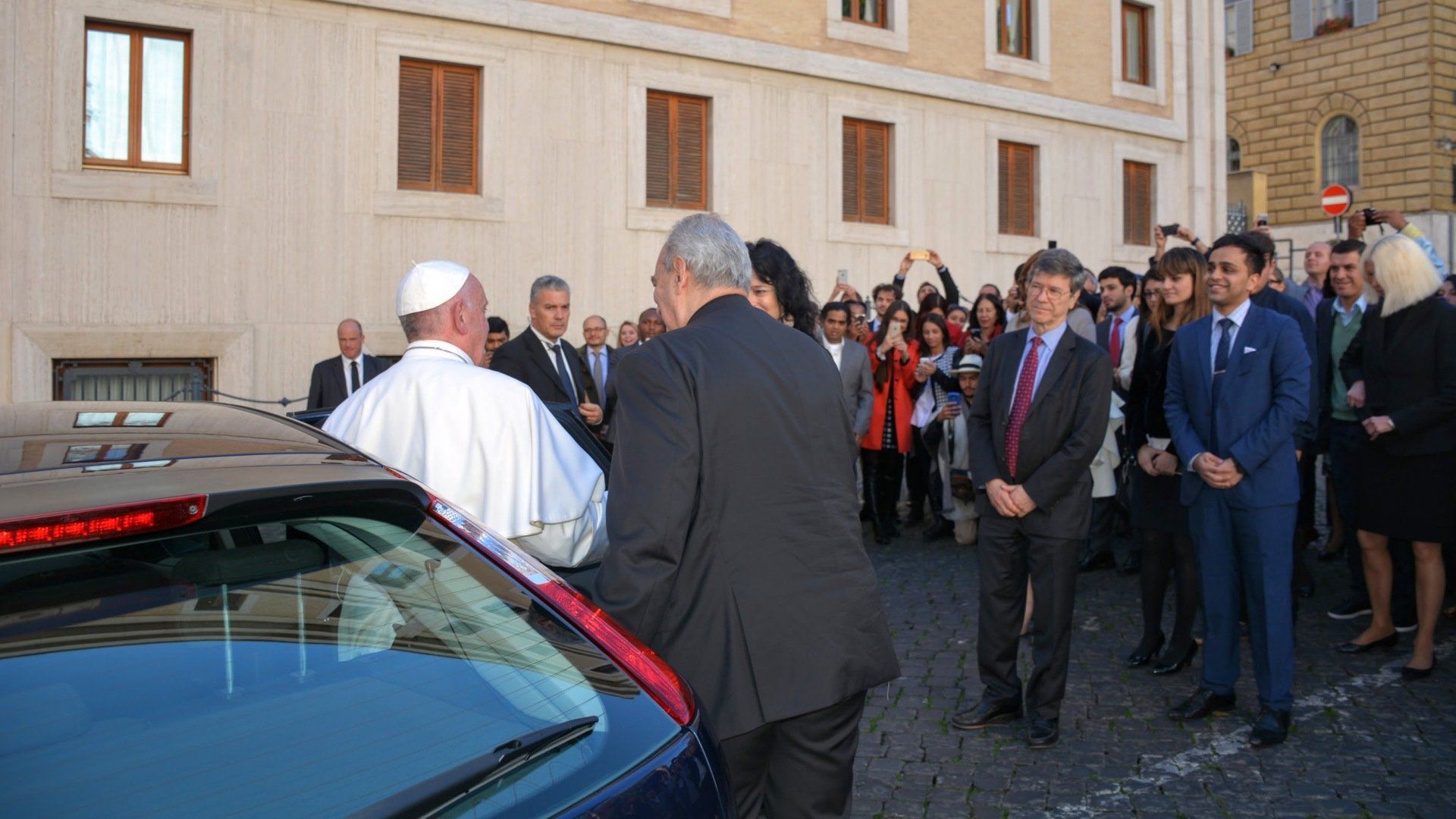 A group of people are standing around a car and talking to each other.