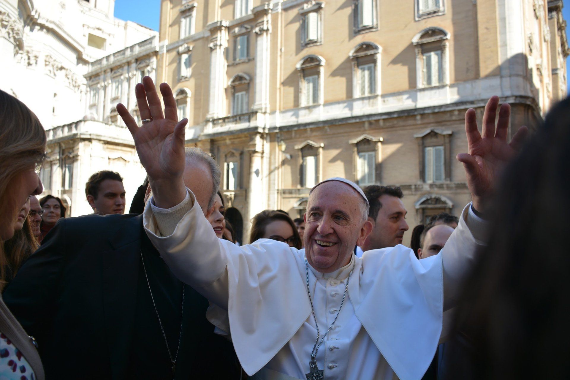 A man in a white robe is waving at a crowd of people.