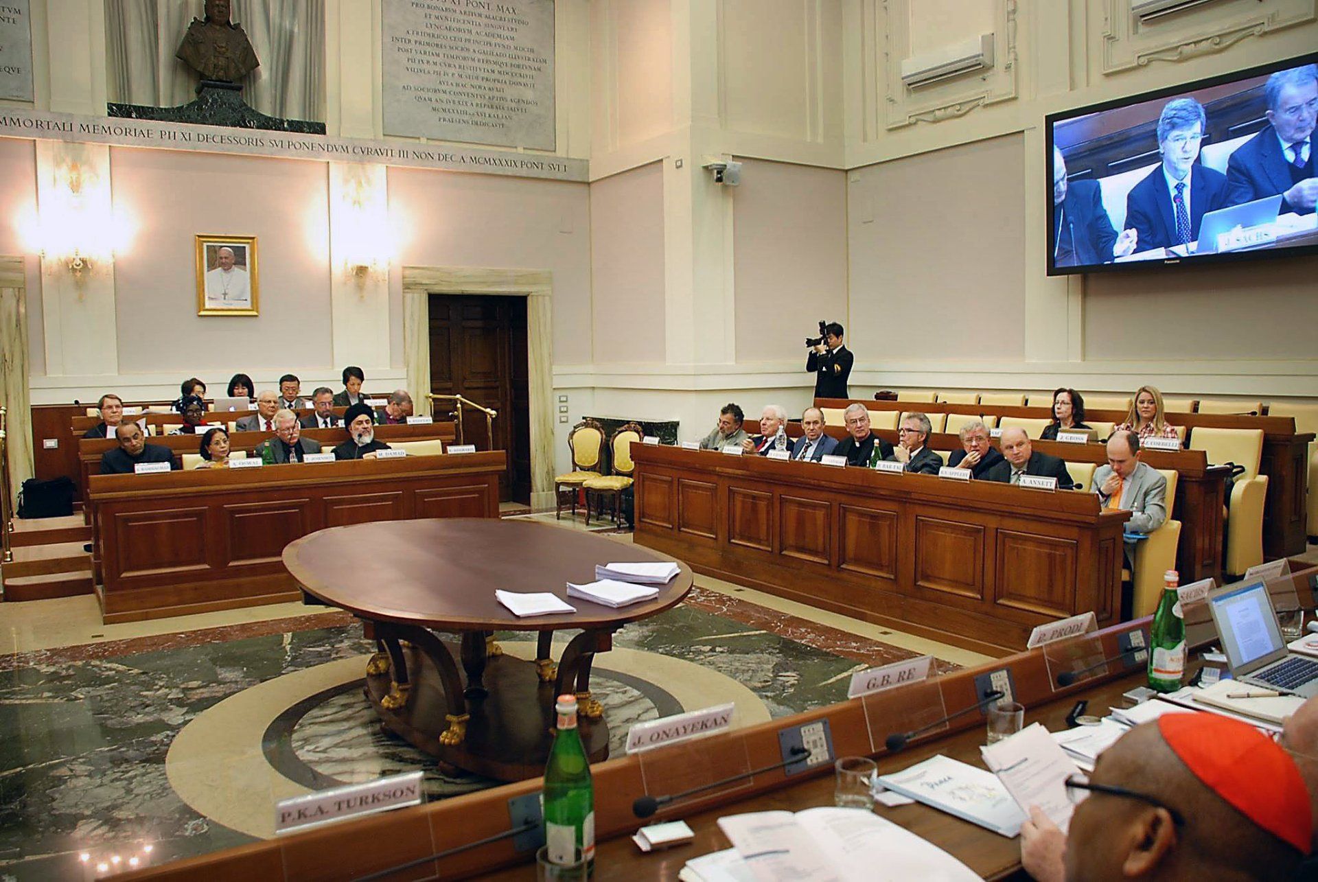 A group of people are sitting at a table in front of a large screen