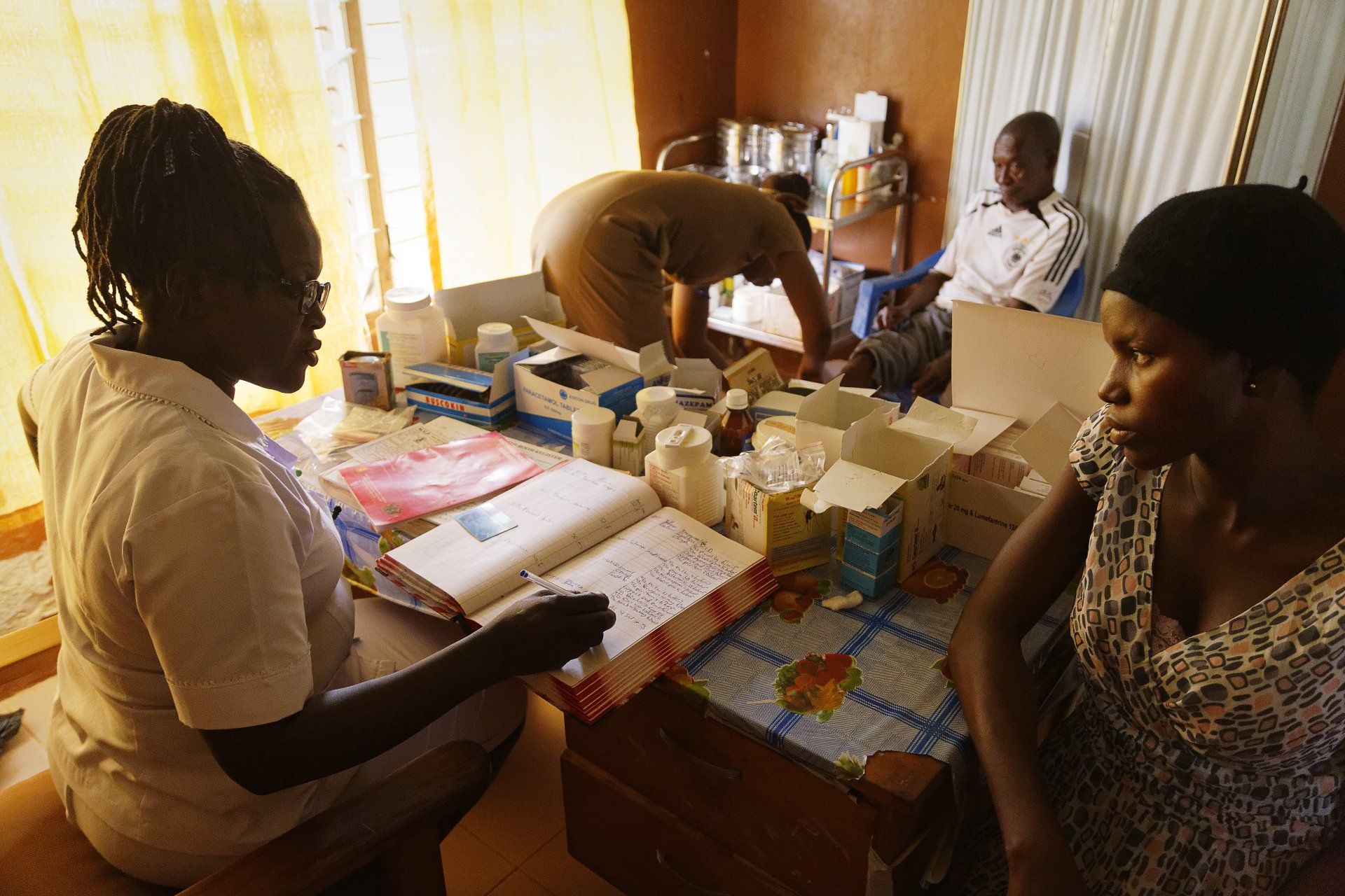 VII Foundation: Two girls looking at a textbook while a women in the back helps and older man