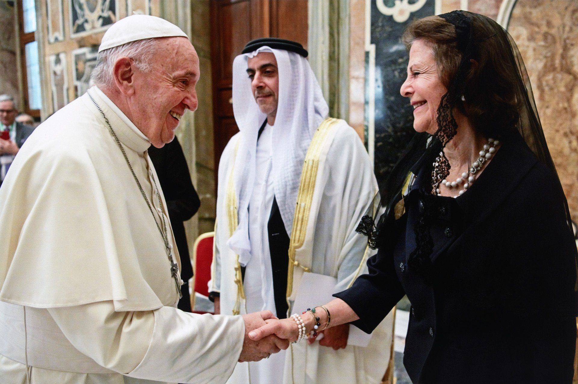The pope and a women wearing all black shacking hands and smiling 