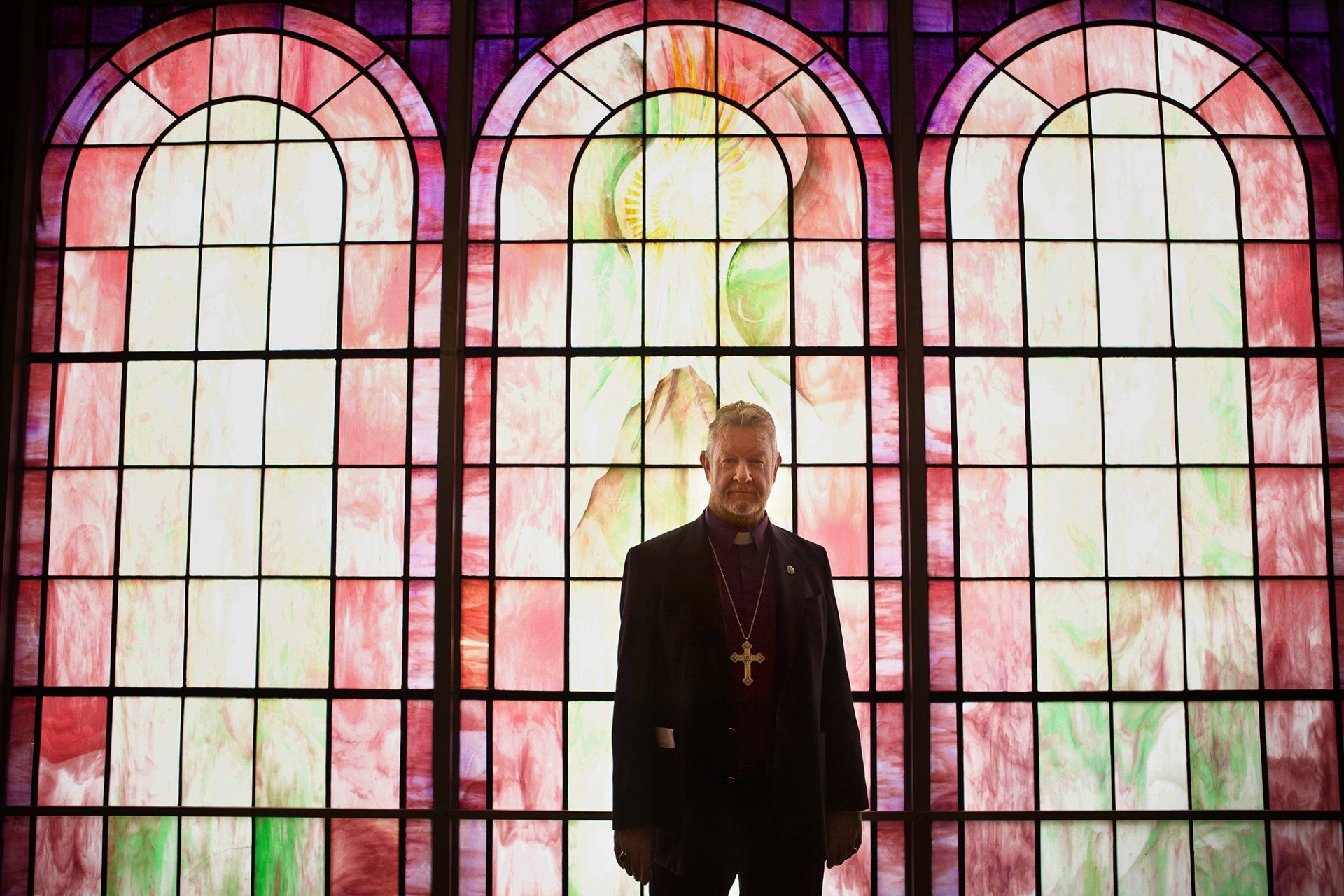 A man is standing in front of a stained glass window.