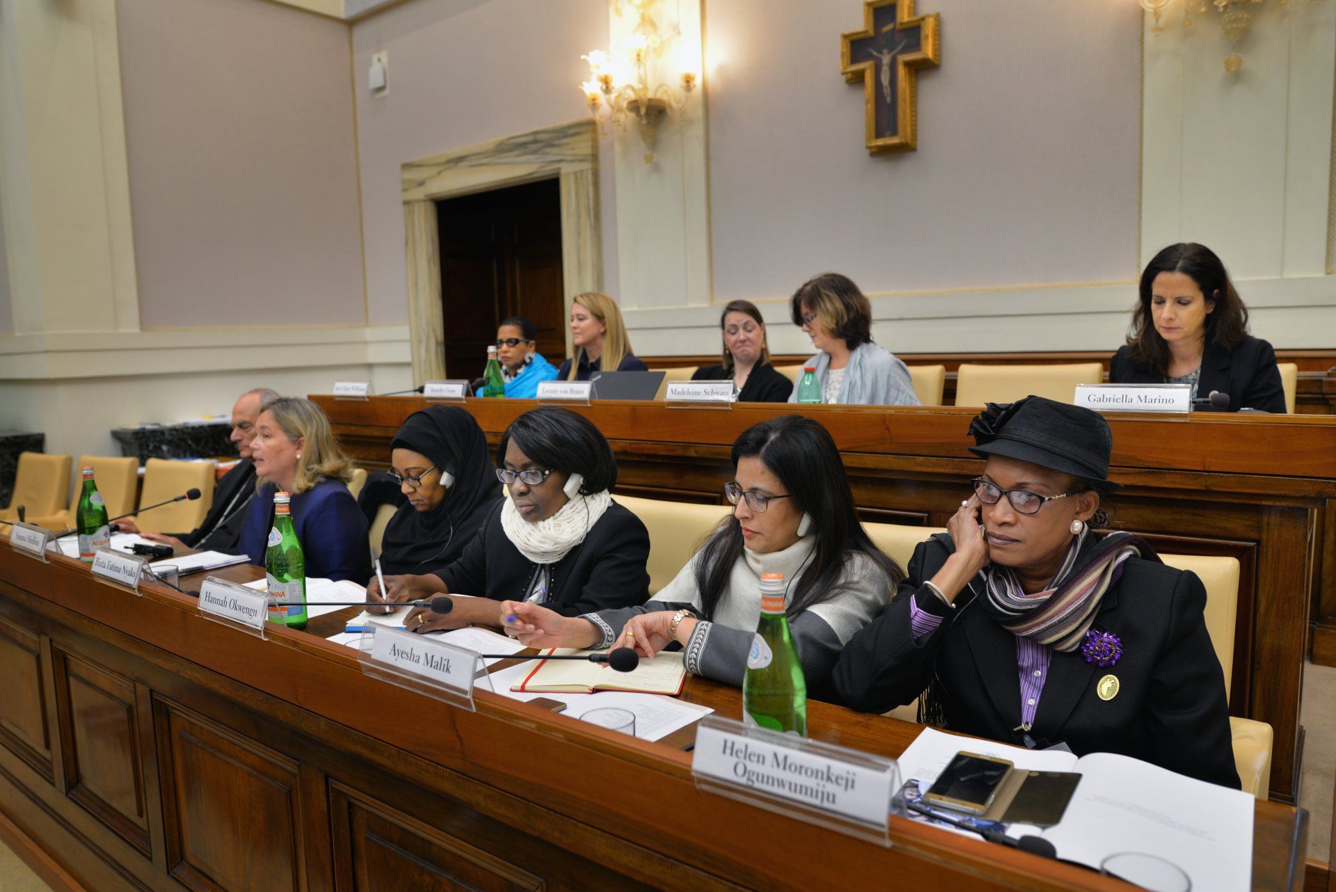 A group of women are sitting at a long table with a cross in the background.