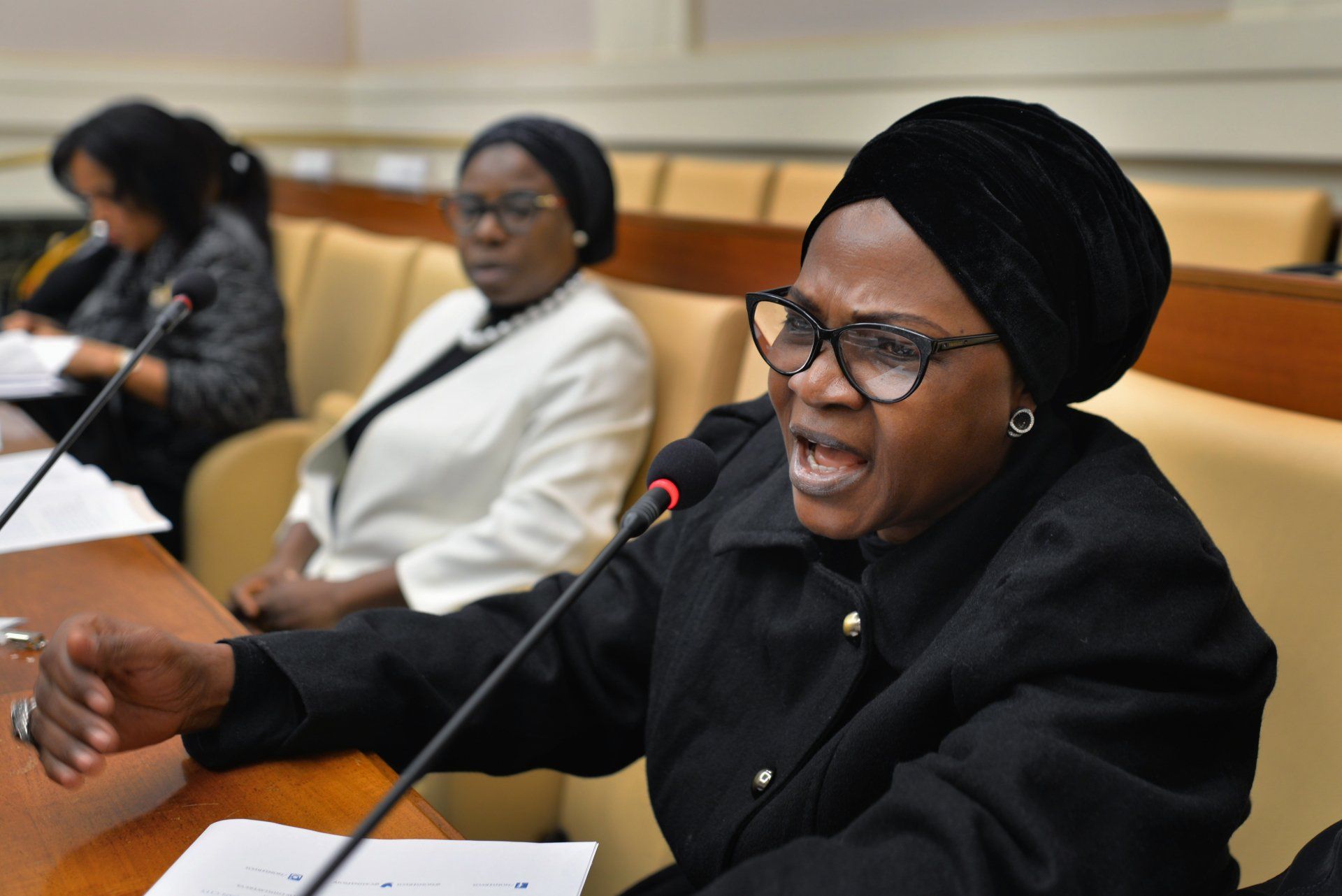 A woman in a black turban is speaking into a microphone