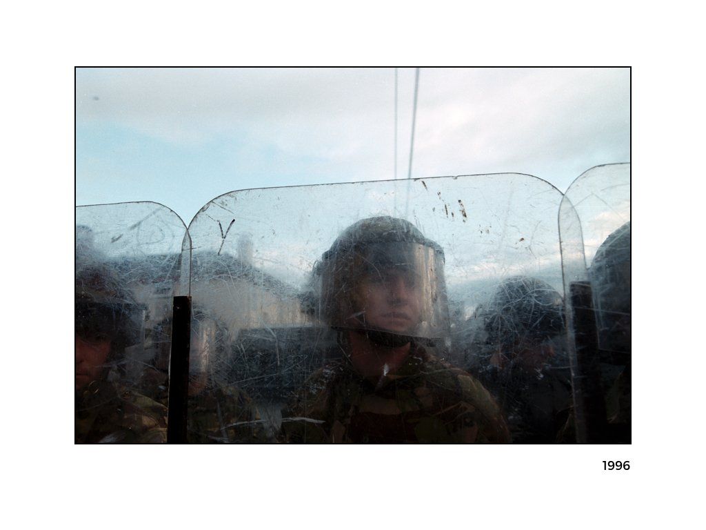 The Peace Project: A women in military gear holding up a clear shield in Northern Ireland 1996