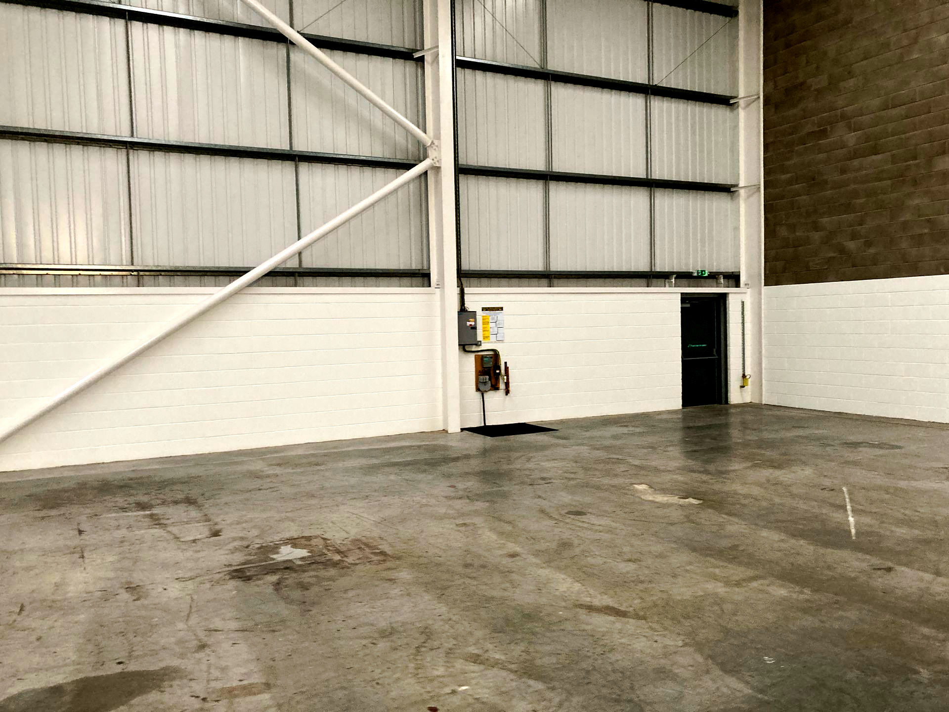 Empty warehouse interior featuring a white brick wall, metal siding, structural beams, a black door, and concrete floors.