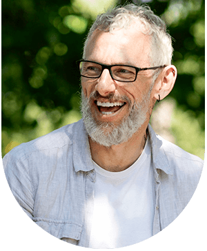 Older man smiling with a sandwich, showcasing the natural look of porcelain veneers at Hampstead Clinic