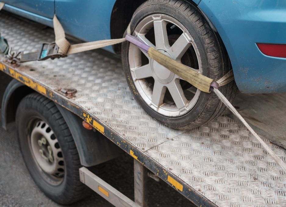 A blue car is being towed by a tow truck.