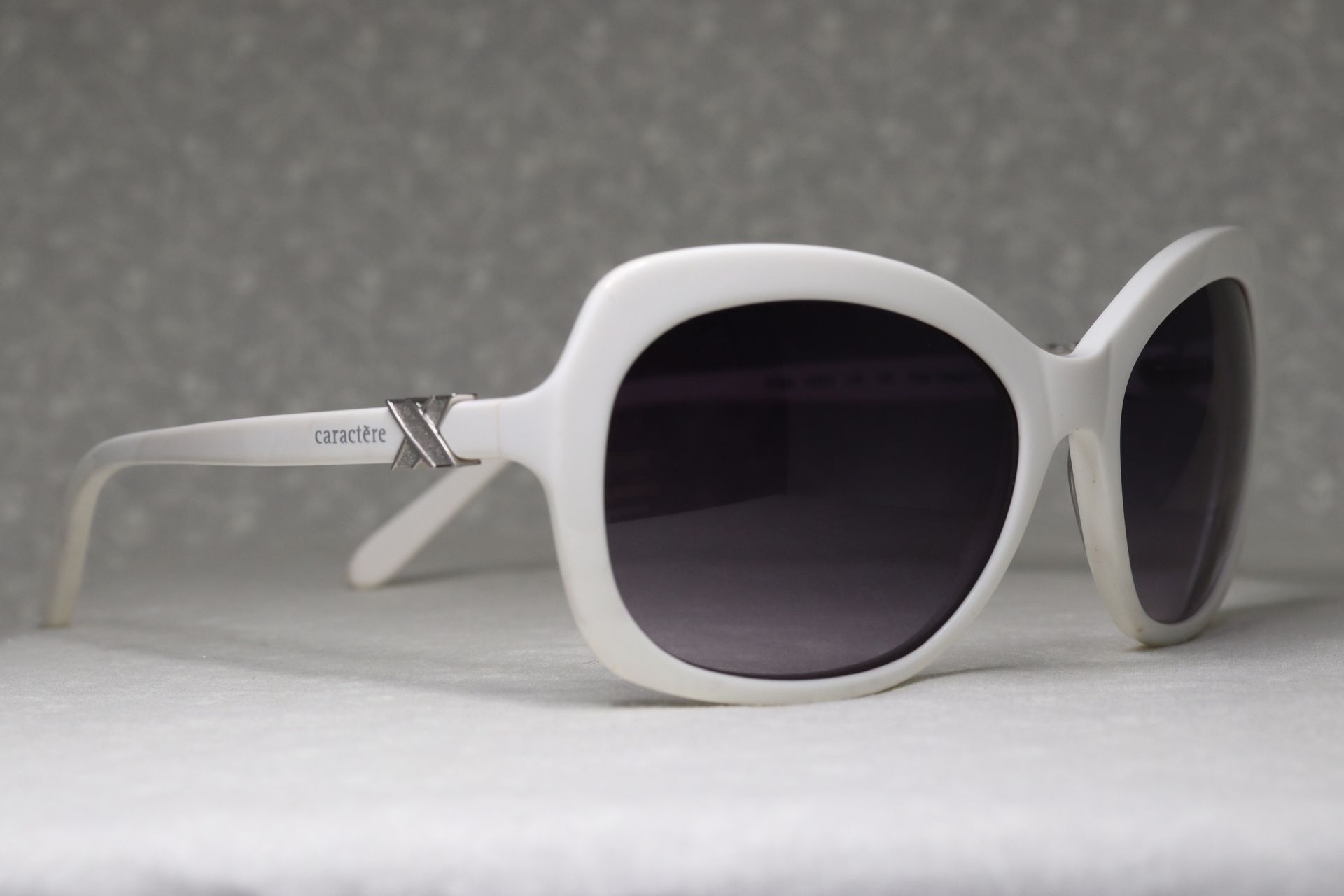 A pair of white sunglasses with black lenses on a white surface.