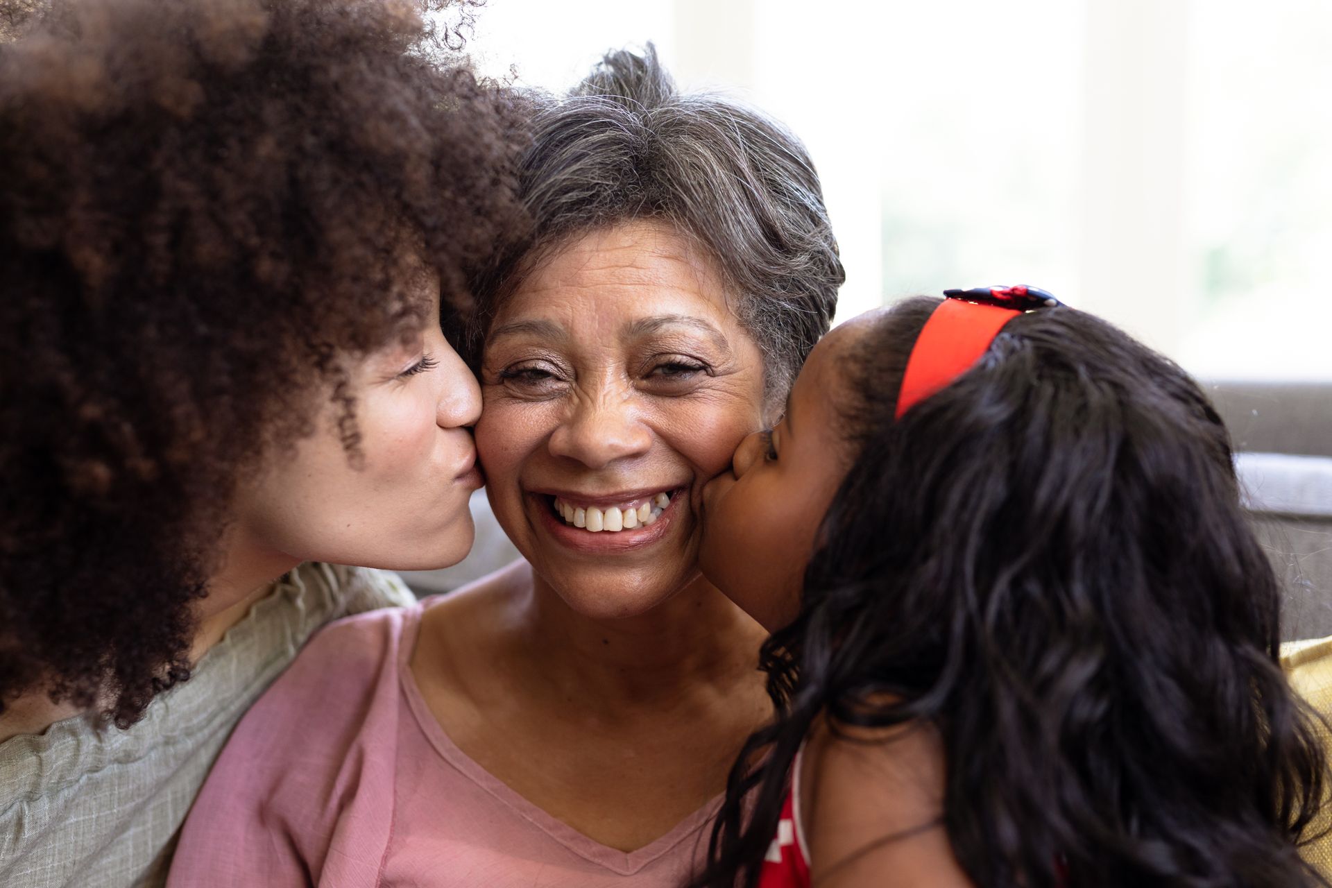 two women and a child are kissing an older woman on the cheek .