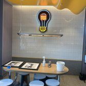 Restaurant interior with a table, stools, and lightbulb-shaped sign.